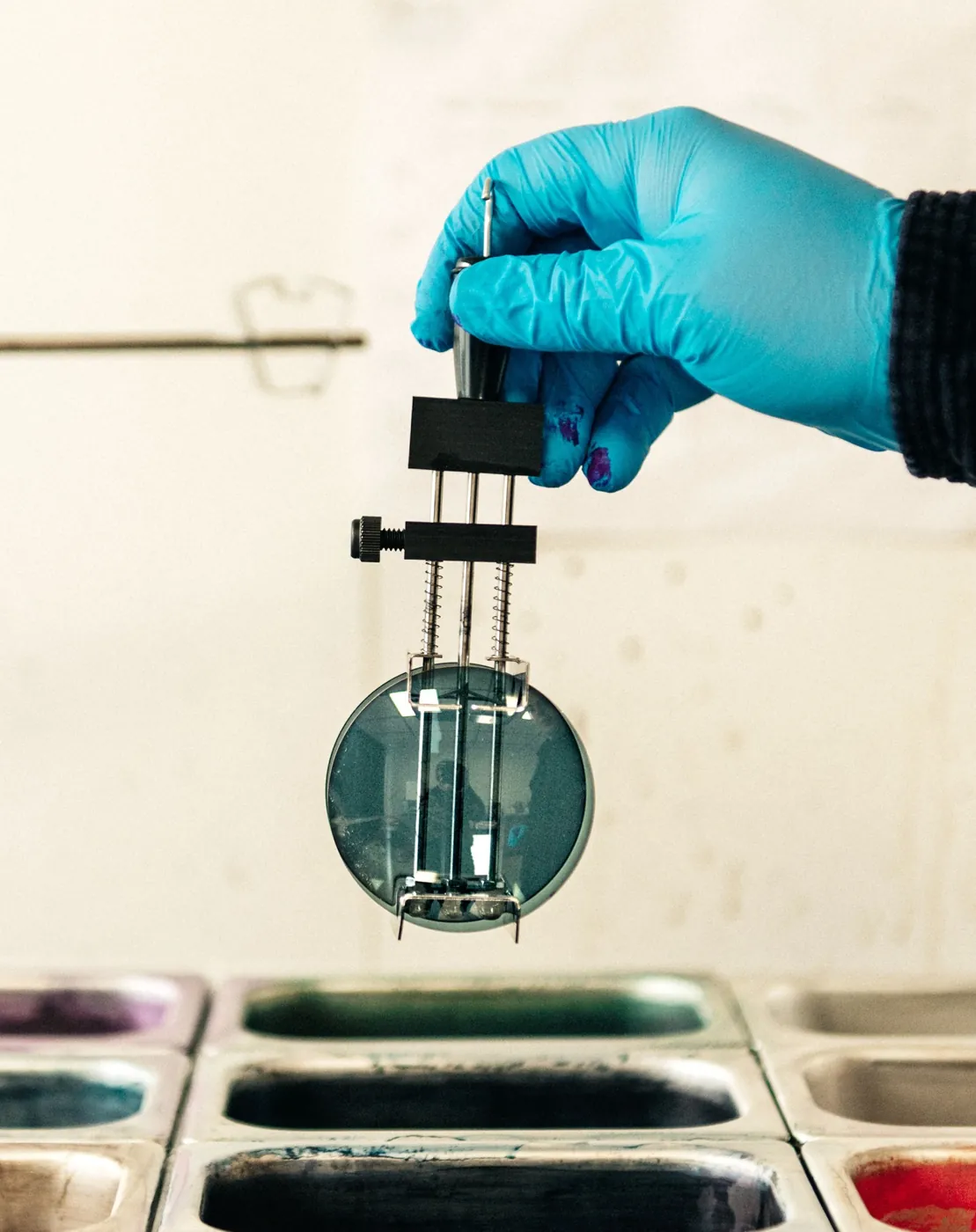 Une main gantée sort un verre teinté des bacs de coloration